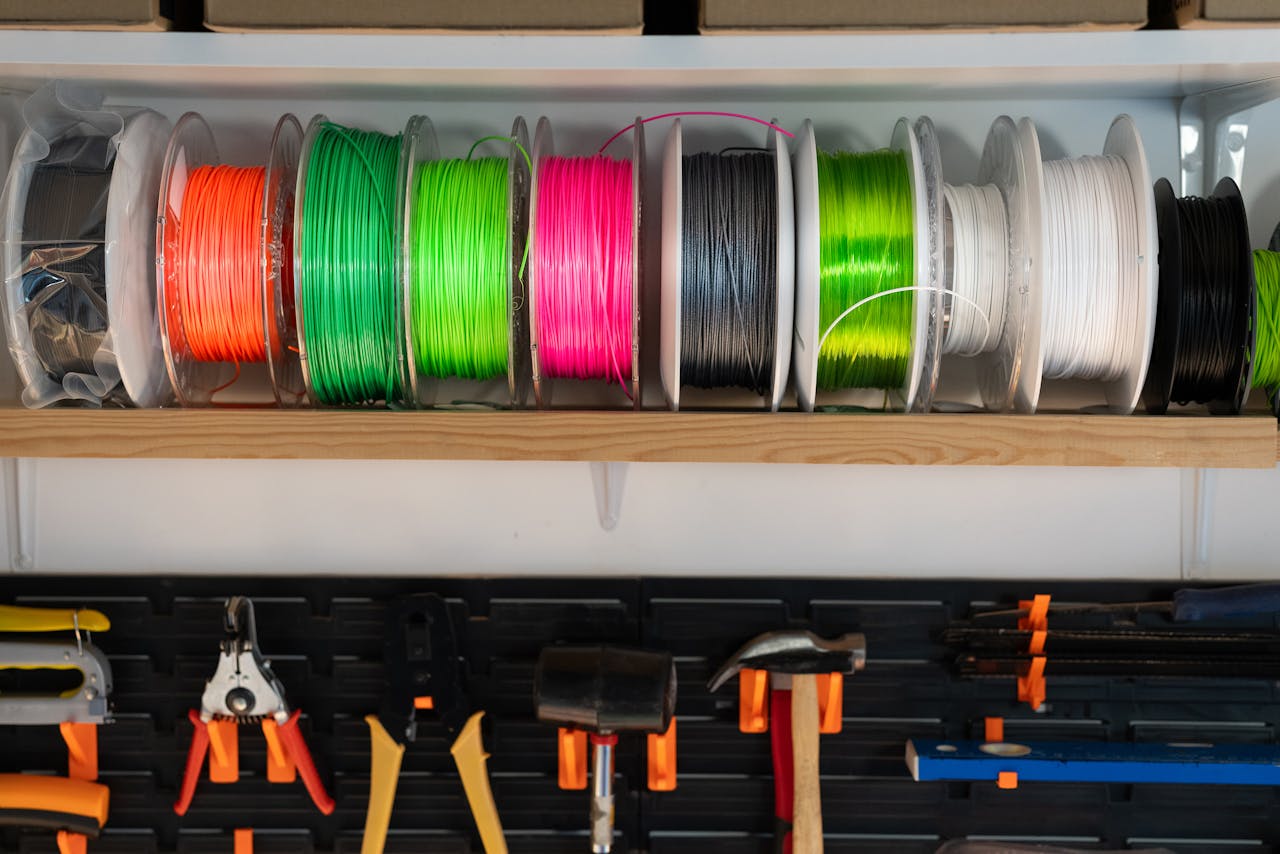 about-01 A variety of colorful filament spools and tools organized on a workshop shelf, ideal for 3D printing enthusiasts.